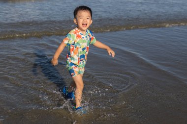 Neşeli bir çocuk, güneşli bir sahilde kumsalda oynar. Yazın kaygısız ruhunu ve açık hava aktivitelerinin neşesini somutlaştırır.