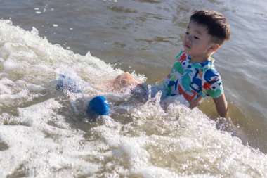 Neşeli bir çocuk, güneşli bir sahilde kumsalda oynar. Yazın kaygısız ruhunu ve açık hava aktivitelerinin neşesini somutlaştırır.