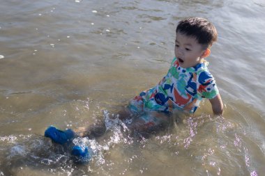 Neşeli bir çocuk, güneşli bir sahilde kumsalda oynar. Yazın kaygısız ruhunu ve açık hava aktivitelerinin neşesini somutlaştırır.
