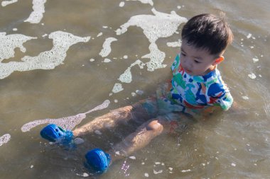 Neşeli bir çocuk, güneşli bir sahilde kumsalda oynar. Yazın kaygısız ruhunu ve açık hava aktivitelerinin neşesini somutlaştırır.
