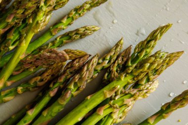 Taze kuşkonmaz, su damlalarıyla durulanır, kesme tahtasının üzerinde..