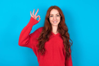 Mavi arka planda kırmızı süveter giyen genç bir kadın. Kolunu tut. Tamam.