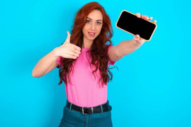 Mavi arka plan üzerinde pembe tişört giyen beyaz saçlı genç bir kadının portresi. Hücrede el ele tutuşmuş, siyah başparmağını kaldırıyor.