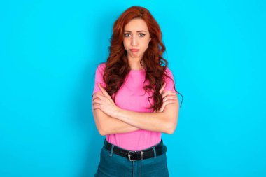 Kasvetli, tatminsiz, beyaz saçlı, pembe tişörtlü, mavi arka planda genç bir kadın. Alnının altından zavallı bir ifadeyle, suratını buruşturuyor.