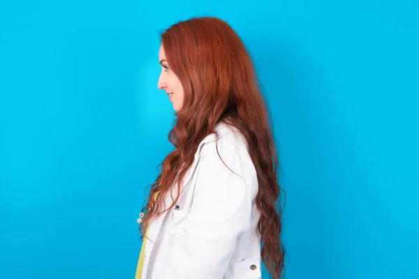 Profile portrait of nice Young redhead caucasian doctor woman over blue background look empty space toothy smile