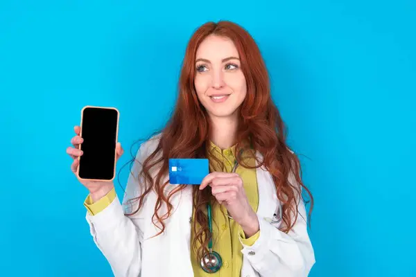 Junge Rothaarige Kaukasische Ärztin Über Blauem Hintergrund Mit Bankkarte Modernes — Stockfoto