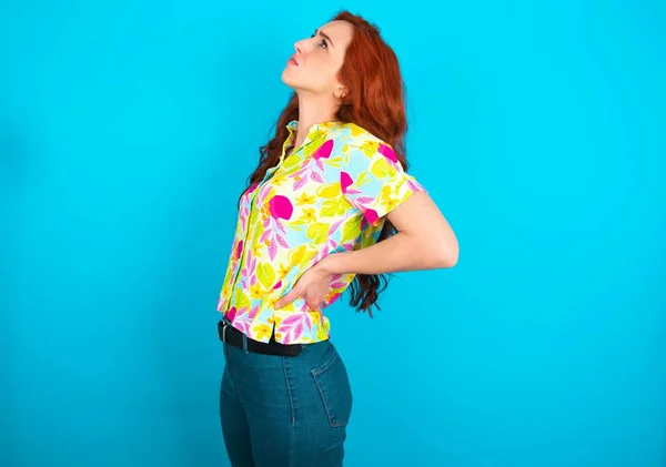 年轻的高加索红头发女人穿着蓝色背景的彩色衬衫 — 图库照片