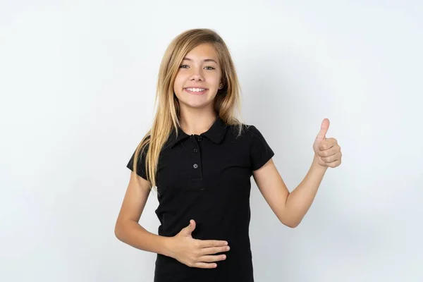 티셔츠를 아름다운 화이트 스튜디오 배경에 긍정적 미소짓는 소녀가 엄지손가락을 줍니다 — 스톡 사진