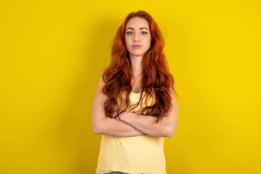 Kendine güveni tam, genç, kızıl saçlı sarı tişörtlü, sarı stüdyo arka planı kolları bağlı. Profesyonel titreşimlerin kendine güvenen pozlarda durduğunu gösterir.