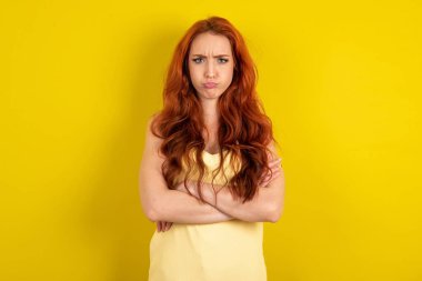 Hüzünlü, genç, kızıl saçlı, sarı tişörtlü, stüdyo sarısı arka planda, alnının altındaki kameraya sefil bir yüz ifadesiyle, mutsuz, suratını buruşturur.