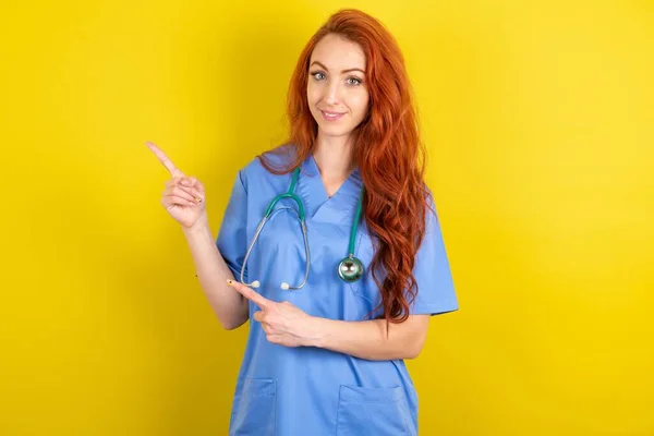 黄色のスタジオの背景の上に若い赤髪の医師の女性コピースペースでのポイントは 広告のための示す正しい方向を与える — ストック写真