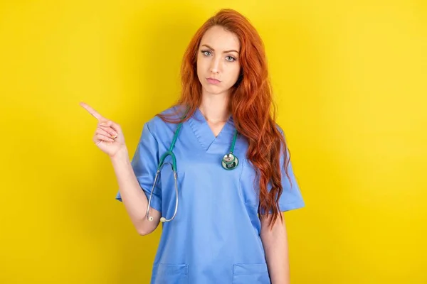Σοβαρή Νεαρή Κοκκινομάλλα Γιατρός Γυναίκα Πάνω Από Κίτρινο Φόντο Στούντιο — Φωτογραφία Αρχείου