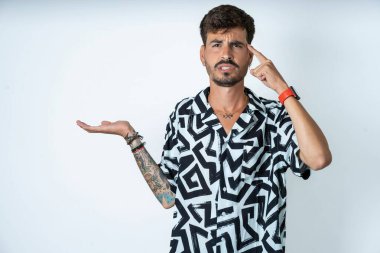 Baskılı tişört giyen genç beyaz bir adam avuç içinin açık olmasından rahatsız ve kafası karışmış bir şekilde fotokopi alanını gösteriyor ve alnını işaret ediyor. Bunu bir düşün..