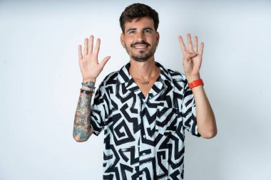 Beyaz gömlekli genç adam dokuz numaralı parmaklarını gösterip işaret ederken kendinden emin ve mutlu bir şekilde gülümsüyor..