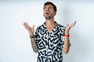 Baskılı tişört giyen genç beyaz adam deli gibi bağırıyor ve agresif bir ifadeyle bağırıyor ve kollarını kaldırıyor. Hayal kırıklığı konsepti.