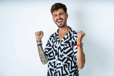 Baskılı tişört giyen genç beyaz adam kolları havada ve gözleri kapalı bir şekilde başarıyı kutluyor ve şaşırıyor. Kazanan konsept.