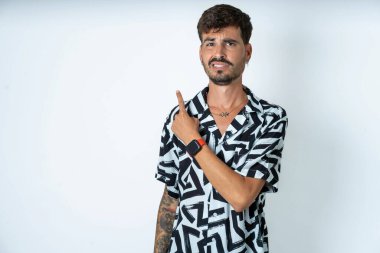 Baskılı gömlek giyen genç beyaz adam endişeli ve endişeli bir kenara işaret ediyor işaret parmağı, endişe ve sürpriz konsept.