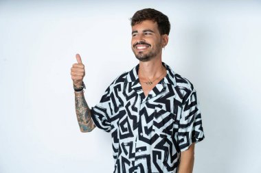 Baskılı tişört giyen genç beyaz adam gururlu görünüyor, gülümsüyor kenarda baş parmak hareketi yapıyor. İyi iş.!