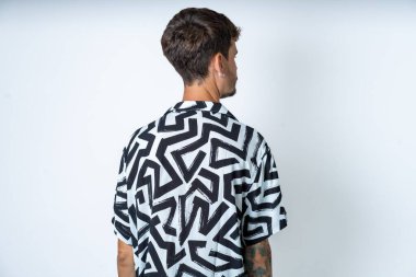 İzole edilmiş beyaz arka planda duran, dövmeli, yazlık tişörtlü genç bir adamın arka tarafı. Stüdyo Çekimi.