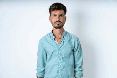 Beyaz arka planda turkuaz gömlek giyen yakışıklı genç adam parmaklarını göstererek reklamını yapıyor, şaşırmış yüz ve ağzını açıyor.