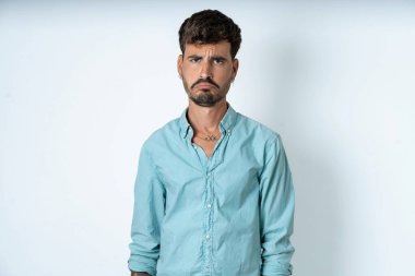 Beyaz arka planda turkuaz gömlek giyen yakışıklı genç adam depresif ve endişeli, sinirli ve korkmuş. Üzücü ifade.