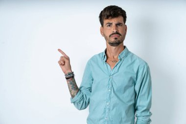 Beyaz arka plan sırıtışları üzerine turkuaz gömlek giyen ciddi yakışıklı genç adam fotokopi alanındaki yüz ifadeleri hoş olmayan bir şey gösteriyor. Şu reklama bak. Büyük fiyat konsepti