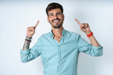 Beyaz arka planda turkuaz gömlek giyen neşeli yakışıklı genç adam saç modelini gösteriyor.