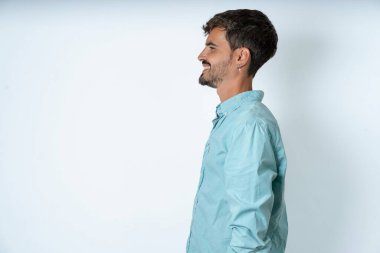 Beyaz arka planda turkuaz gömlek giyen yakışıklı genç bir adamın profil portresi boş dişli bir gülümseme.