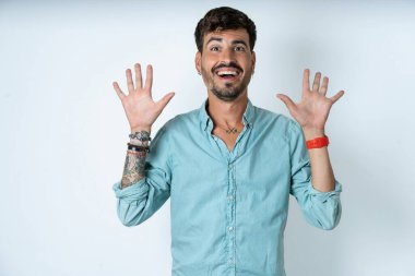 Beyaz arka planda turkuaz gömlek giyen yakışıklı genç adam harika bir sonuç elde ettikten sonra ağzını ve kollarını açar.