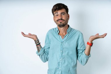 Dikkatsiz, yakışıklı, turkuaz gömlek giyen beyaz arka plan omuzlarını silkeleyen genç bir adam..