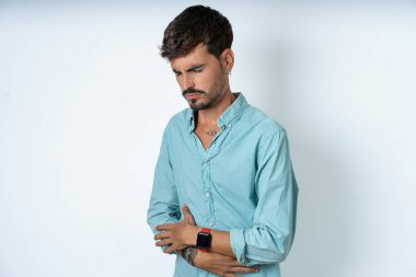 Beyaz arka planda turkuaz gömlek giyen yakışıklı genç adamın midesi ağrıyordu.