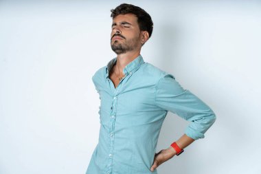Beyaz arka planda turkuaz gömlek giyen yakışıklı genç adam sırt ağrısı çekti.