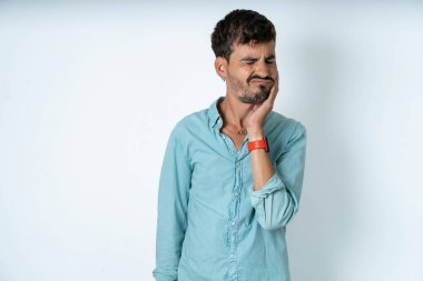 Beyaz arka planda dişleri ağrıyan turkuaz gömlek giyen yakışıklı bir genç.