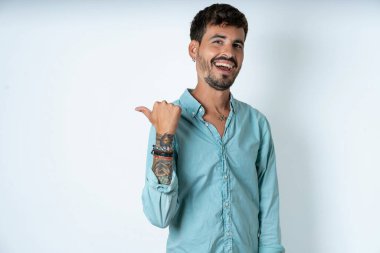 Etkileyici yakışıklı genç adam, beyaz arka plan noktasının üzerinde turkuaz gömlek giyiyor.