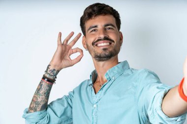 Beyaz arka planda turkuaz gömlek giyen oldukça neşeli genç bir adamın portresi selfie şovunu sembolize ediyor.