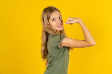Sarı arka plan üzerinde haki rengi bluz giyen güçlü, neşeli sarışın küçük kızın portresi kasları gösteriyor..
