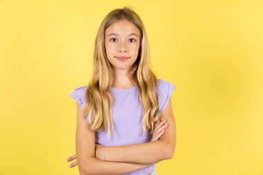 Kendine güvenen, ciddi, sakin, mor tişörtlü, sarı arka planda kolları bağlı sarışın bir kız. Profesyonel titreşimlerin kendine güvenen pozlarda durduğunu gösterir.