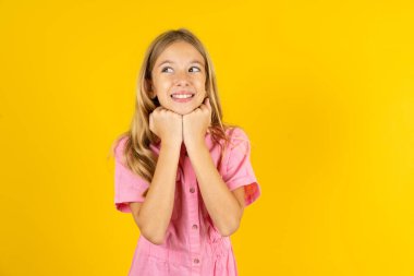 Sarı arka planda pembe ceket giyen kız çene altında el ele tutuşuyor, yabancılardan samimi sözler duymak güzel.