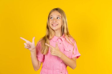 İki eliyle sarı arka plan noktalarının üzerine pembe ceket giyen iyimser kız boş bir yere bakıyor..