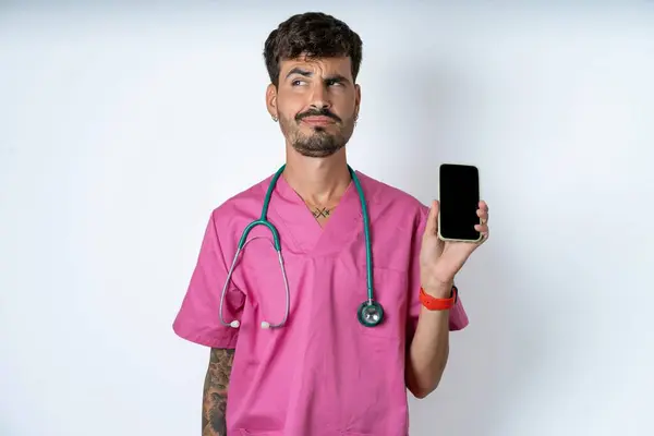 白底身穿外科制服的英俊护士拿着新手机 看起来很神秘 旁边是现代手机的空白展示 — 图库照片