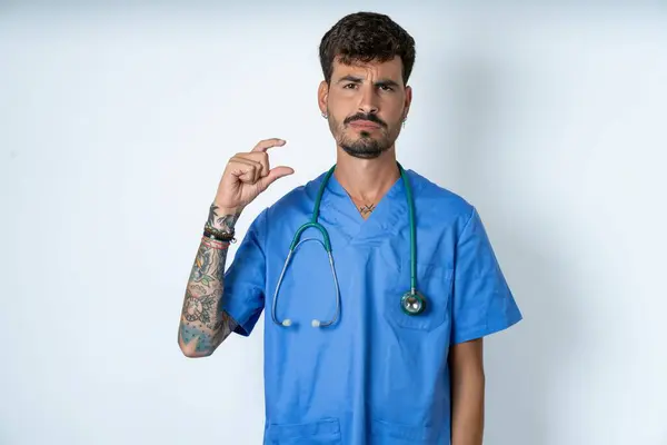 Ontevreden Knappe Verpleegkundige Man Draagt Chirurg Uniform Witte Achtergrond Vormen — Stockfoto