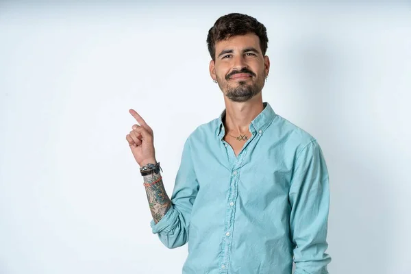 一个英俊的年轻人穿着蓝绿色的衬衫 站在白色的背景点上 站在空白的地方展示广告 人与晋升概念 — 图库照片
