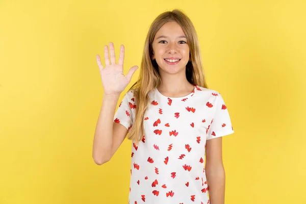 黄色い背景にポルカのドットシャツを着て 自信と幸せを笑いながら指番号5を指で指で指で指で指で指を指さしている白人の少女 — ストック写真