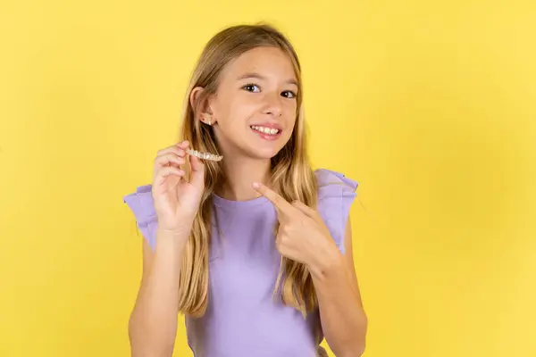 Blonde Girl Wearing Violet Shirt Yellow Background Holding Invisible Aligner — Stock Photo, Image