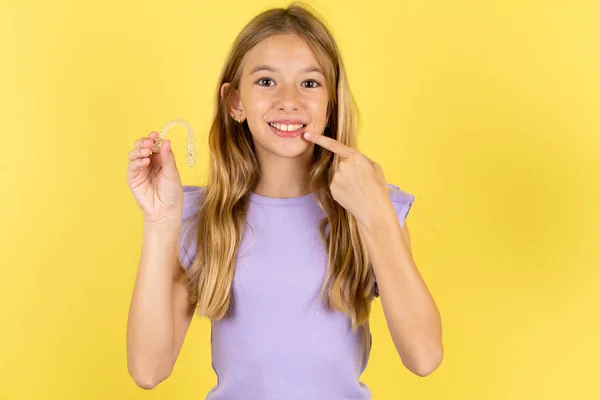 Menina Loira Vestindo Camiseta Violeta Sobre Fundo Amarelo Segurando Aligner — Fotografia de Stock