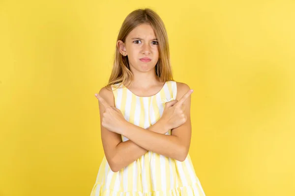 Serieus Meisje Draagt Gele Jurk Gele Achtergrond Kruist Handen Punten — Stockfoto