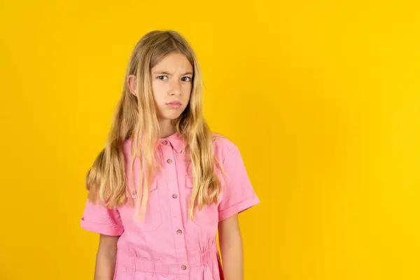 黄色いバックグラウンドの上にピンクのジャケットを着用している不満の少女は 不幸なことにいくつかの問題があると感じています ネガティブな感情と感情の概念 — ストック写真
