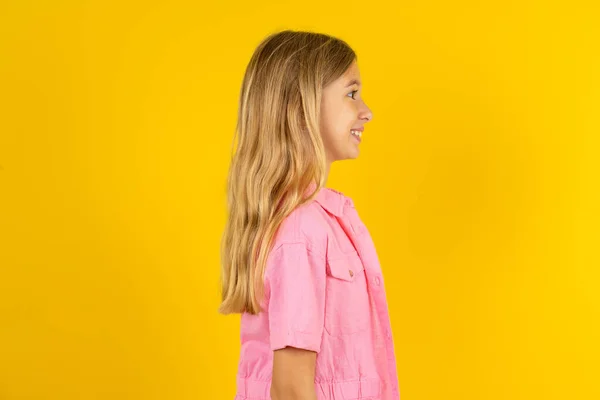黄色い背景の上にピンクのジャケットを着ている素敵な女の子のプロフィールの肖像画は空のスペースを見ます 微笑みます — ストック写真