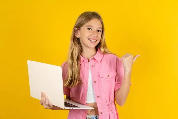 穿着粉色夹克的女孩 背景是黄色的 方向是空旷的 手持笔记本电脑 — 图库照片