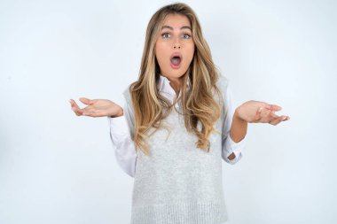 Hayal kırıklığına uğramış güzel İspanyol iş kadını beyaz arka planda şaşkın ve tereddütlü hissediyor, şaşkınlıkla omuz silkiyor, ağzını açık tutuyor, ne yapacağını bilmiyor..